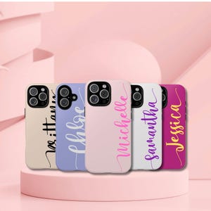 May include: Five different phone cases with names printed on them. The cases are in various colors, including pink, white, purple, and blue. The names are written in a cursive font.