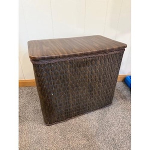 May include: A brown wicker laundry hamper with a wooden top. The hamper has a rectangular shape and a woven texture. The lid is a darker shade of brown than the hamper's body. The hamper is designed for storing laundry.