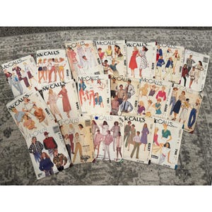 May include: A collection of vintage McCall's sewing patterns. The patterns feature illustrations of various clothing designs, including dresses, suits, and separates. The covers display a range of colors and styles, showcasing fashion trends.