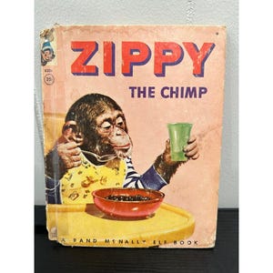 May include: Vintage children's book titled "ZIPPY THE CHIMP." The cover features a chimpanzee eating from a bowl and holding a green glass. The book has a pink cover with red lettering and a yellow tray.