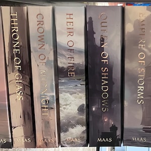 Könnte beinhalten: Eine Sammlung von acht gebundenen Büchern, die nebeneinander angeordnet sind und illustrierte Buchrücken mit den Titeln The Assassin's Blade, Throne of Glass, Crown of Midnight, Heir of Fire, Queen of Shadows, Empire of Storms, Tower of Dawn und Kingdom of Ash zeigen.