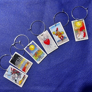 May include: Six silver charm bracelets with colourful tarot card charms. The charms feature images of The Sun, The Moon, The Knight of Swords, The Emperor, and two other cards.