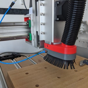 Könnte beinhalten: Nahaufnahme einer CNC-Maschine mit einem Staubabsaugsystem. Die Maschine hat eine rote und graue Staubabsaugbürste, die an einem schwarzen Schlauch befestigt ist. Die Bürste befindet sich über einem Stück Holz.