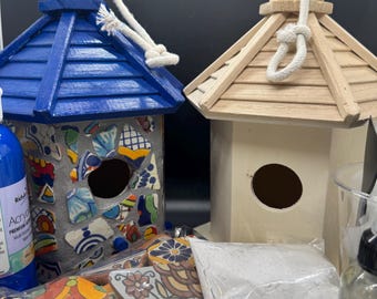 Könnte beinhalten: Zwei Vogelhäuser, eines blau und eines aus Naturholz, mit Seilaufhängern. Das blaue Vogelhaus hat ein Mosaikdesign. Bastelbedarf umfasst Farbe, Fliesen und einen Beutel mit Pulver. Ein DIY-Vogelhaus-Kit.