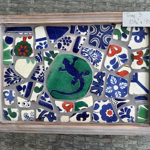 May include: A rectangular serving tray with a mosaic tile design. The tray features a wooden frame and black handles. The mosaic is composed of blue, white, green, and red tiles, with a central green tile featuring a blue lizard. The tray measures 13 3/4 x 9 1/2 inches.