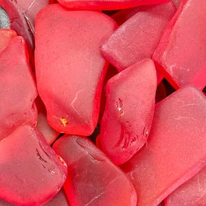 Puede incluir: Primer plano de un montón de vidrio de mar rojo. El vidrio es liso y translúcido, con una variedad de formas y tamaños.