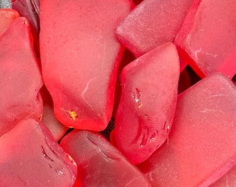 May include: A close-up of a pile of red sea glass. The glass is smooth and translucent, with a variety of shapes and sizes.