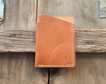 May include: A brown leather wallet with a rooster logo and a stitched edge.