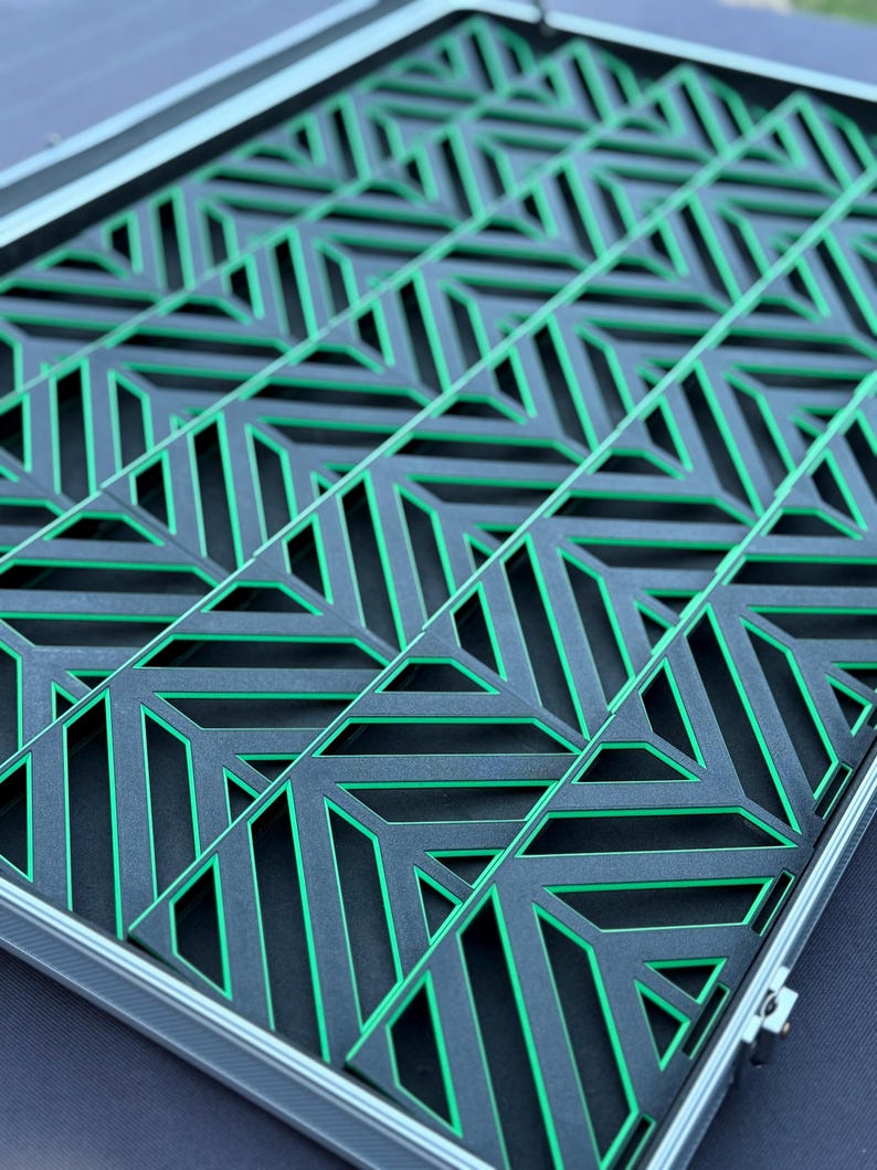May include: A geometric design in a rectangular frame. The design features a repeating pattern of black shapes with green accents. The frame is silver. The overall aesthetic is modern and abstract.