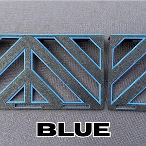 May include: Two geometric, rectangular objects with a black base and blue accents. The design features diagonal lines and a peace symbol shape. The word "BLUE" is written in bold, white letters.