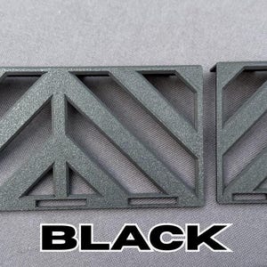 May include: Two black, geometric, metal pieces with a diagonal pattern. The larger piece has a peace sign design in the center. The word "BLACK" is printed in bold, white letters at the bottom.