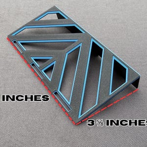May include: A black and blue geometric design, measuring 7 inches by 3 5/8 inches. The design features a series of angled lines and shapes with blue accents. The edges are outlined in red.