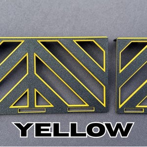 May include: Two black metal decorative panels with yellow diagonal stripes and geometric cutouts. The word "YELLOW" is displayed in bold white letters at the bottom of the image. The panels are on a gray background.