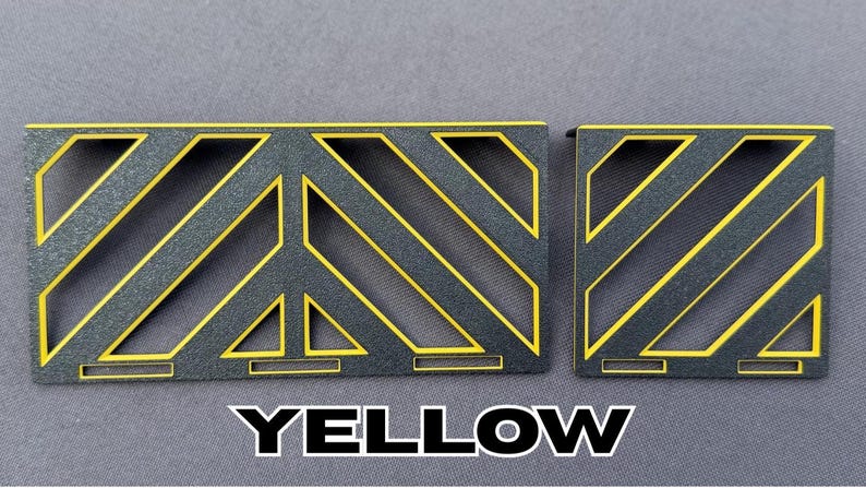 May include: Two black metal decorative panels with yellow diagonal stripes and geometric cutouts. The word "YELLOW" is displayed in bold white letters at the bottom of the image. The panels are on a gray background.