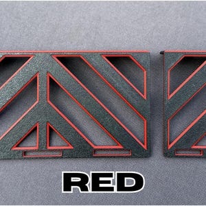 May include: Two rectangular, geometric-patterned objects with a black base and red accents. The word "RED" is displayed in a white font with a black outline at the bottom of the image. The objects have a textured appearance.