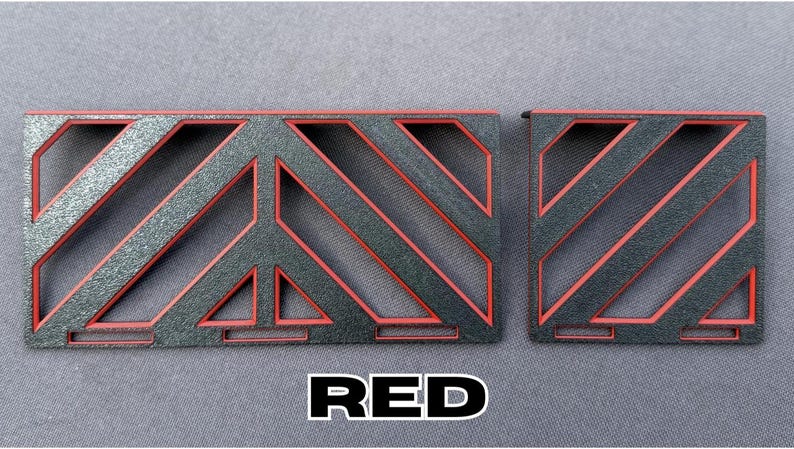 May include: Two rectangular, geometric-patterned objects with a black base and red accents. The word "RED" is displayed in a white font with a black outline at the bottom of the image. The objects have a textured appearance.