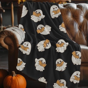 Peut inclure: Une couverture en polaire noire avec un motif répétitif de fantômes blancs lisant des livres. Les fantômes tiennent des livres ouverts avec des pages orange.