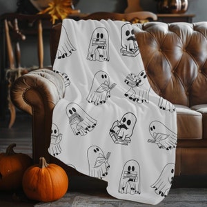 Peut inclure: Jeté blanc avec un motif répété de fantômes lisant des livres. Les fantômes sont noirs et blancs et ont un design simple.