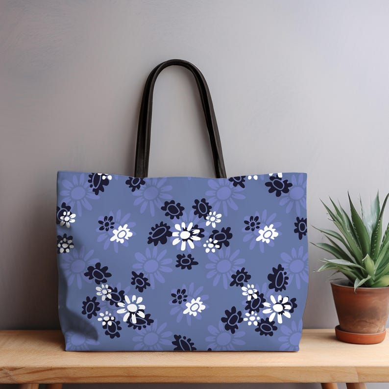 May include: A tote bag with a blue floral pattern. The bag features a repeating design of white, navy, and light blue flowers. It has black handles and is sitting on a wooden surface.