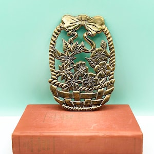 Pode incluir: Uma decoração de parede de metal dourado com uma cesta cheia de flores e um laço no topo.