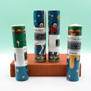 May include: Four rolls of vintage wallpaper border, each with unique designs. The rolls feature illustrations of cowboys, stars, and geometric patterns. The rolls are displayed on a brown book, with text visible on the labels.