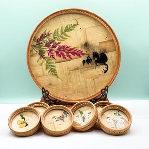 May include: A set of six round bamboo coasters with pressed flower and butterfly designs. The coasters are arranged in a circle around a larger, similar bamboo tray with a pressed fern and butterfly design.