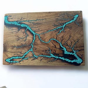 May include: A wooden wall art piece with a turquoise blue resin design resembling a river or stream. The resin is embedded in the wood and has a natural, organic look.