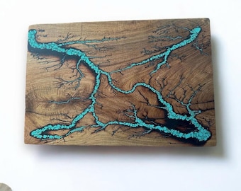 Può includere: Un'opera d'arte da parete in legno con un design in resina blu turchese che ricorda un fiume o un ruscello. La resina è incorporata nel legno e ha un aspetto naturale e organico.