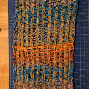 May include: A woven rug with a brown, blue, orange, and pink pattern. The rug is made of natural fibers and has a textured surface.