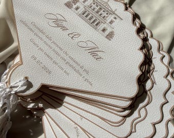 May include: A stack of white, shell-shaped paper fans with scalloped edges and a metallic copper trim. Each fan features a brown ink illustration of a villa, the names "Asya & Max," Italian text, and the date "09.07.2026." A white tassel is attached.