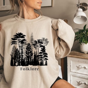 May include: A beige sweatshirt with a black silhouette of a forest and the word "Folklore" printed on the front.