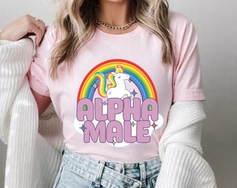 May include: Pink t-shirt with a rainbow and a unicorn graphic. The text "ALPHA MALE" is printed in pink letters on the shirt.