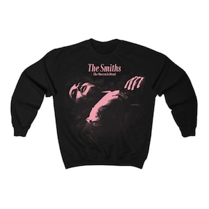 May include: Black sweatshirt featuring the album art from The Smiths' "The Queen is Dead." The design includes a pink image of a person and the band's name and album title in pink text.