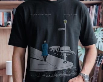 May include: A black t-shirt featuring a graphic illustration of a person in a blue coat walking down a street at night. The design includes a street lamp, a car, and the text New York, December 29th, 1971, Clinton St, and Sincerely, L. Cohen.