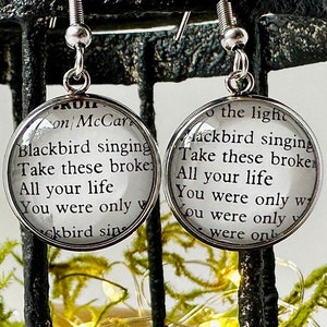 May include: A pair of silver earrings with round glass charms featuring the lyrics "Blackbird singing Take these broken All your life You were only w ckbird sing" and "the light ackbird singing Take these broken All your life You were only w ou were only were onb".