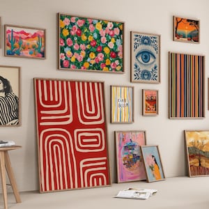 May include: A collection of framed art prints in various sizes and styles, including floral, abstract, and portrait designs. The color palette includes red, blue, yellow, and green. The prints are displayed on a neutral wall, with a wooden stool in the foreground.