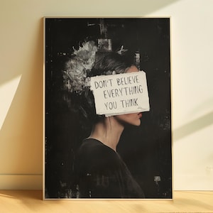 May include: A black and white poster with a woman's face partially obscured by a piece of paper with the text "Don't believe everything you think".