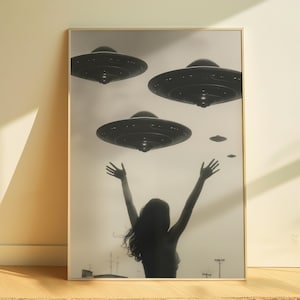 Puede incluir: Una fotografía en blanco y negro de una persona con los brazos en alto, mirando hacia arriba a cuatro platillos volantes. Los platillos están silueteados contra un cielo gris claro.