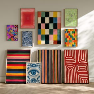Op de afbeelding: Een verzameling ingelijste kunstdrukken met diverse abstracte ontwerpen. De prints tonen geometrische patronen, strepen en oogmotieven in een reeks kleuren, waaronder rood, blauw, geel en groen. Het kunstwerk wordt op een neutrale muur getoond.