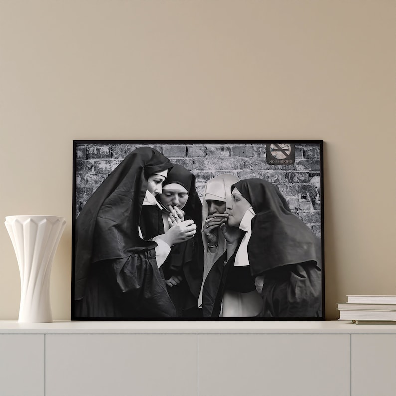 May include: Black and white photograph of four nuns in habits smoking cigarettes. The photo is framed and hanging on a wall.