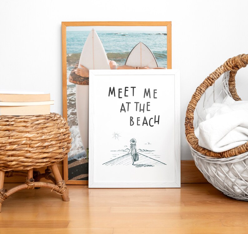 May include: White framed print with the text "Meet me at the beach" and a black and white illustration of a person walking on a beach with a suitcase.