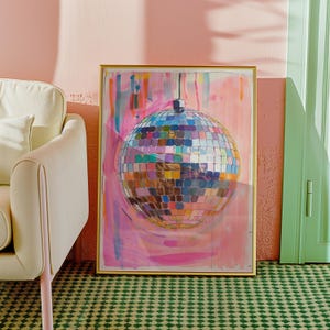 May include: A framed artwork depicting a disco ball with a mosaic design in various colours. The artwork has a gold frame and is set against a pink and white abstract background. The image is in a room with a green patterned carpet and a cream-coloured chair.
