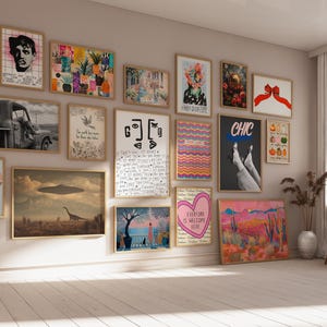 May include: A gallery wall featuring a collection of framed art prints in various sizes and styles, including illustrations of a truck, a dinosaur with a UFO, abstract shapes, a heart, a red bow, and text-based designs, arranged on a beige wall.