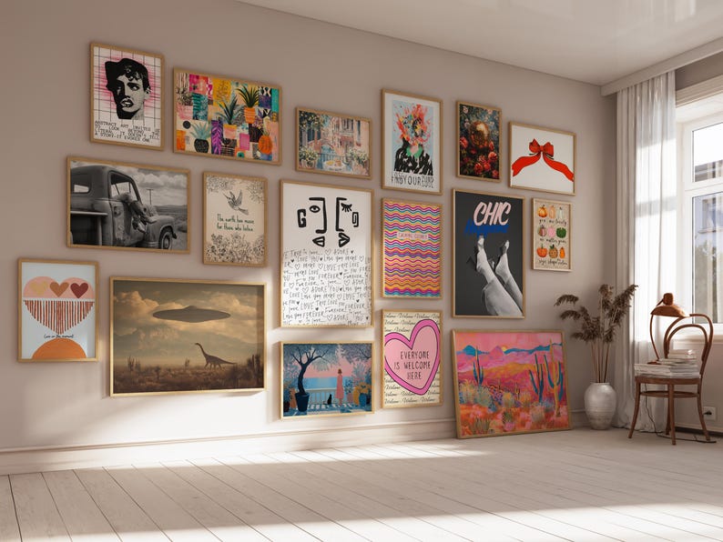May include: A gallery wall featuring a collection of framed art prints in various sizes and styles, including illustrations of a truck, a dinosaur with a UFO, abstract shapes, a heart, a red bow, and text-based designs, arranged on a beige wall.