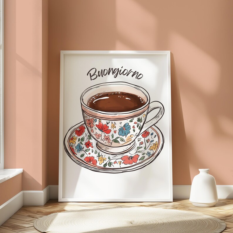 K&ouml;nnte beinhalten: Ein wei&szlig;er gerahmter Druck mit dem Text "Buongiorno" in schwarzer Schrift. Der Druck zeigt eine farbenfrohe, floral gemusterte Teetasse und Untertasse mit einer braunen Fl&uuml;ssigkeit darin.