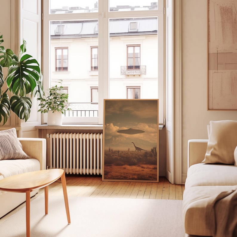 May include: A framed art print depicts a surreal landscape with a dinosaur and a UFO under a cloudy sky. The artwork has a vintage aesthetic, with warm, earthy tones. The print is displayed in a bright, modern living room setting.