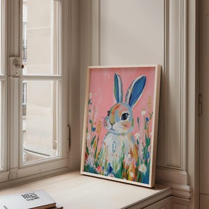 May include: A framed painting of a colorful rabbit with blue ears, surrounded by flowers on a pink background.