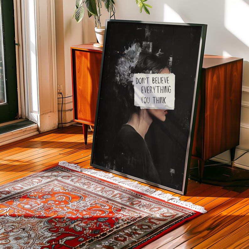 May include: Black and white art print featuring a woman's face with a piece of paper covering her eyes. The paper has the text "Don't believe everything you think" written on it.