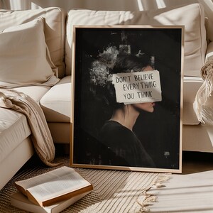 May include: A black and white abstract art print with a woman's face partially obscured by a piece of paper with the text "Don't believe everything you think".