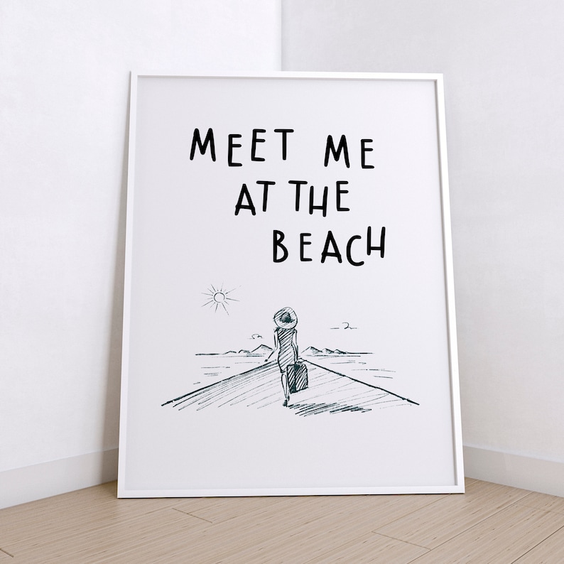 May include: A white framed print with the text "Meet me at the beach" in black. A black and white sketch of a person walking towards the beach with a suitcase is below the text.